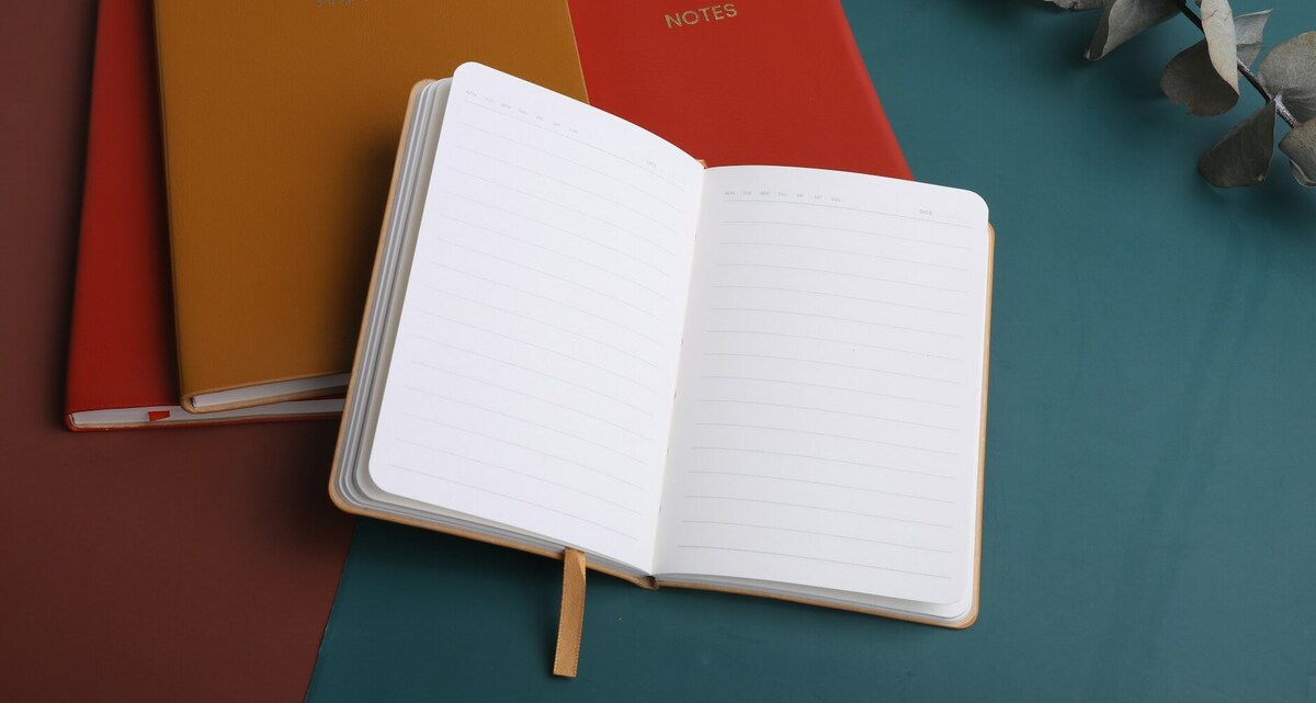 A notebook on a table next to a book, reflecting a sophisticated and timeless design approach. Photo by shen tony on Unsplash.
